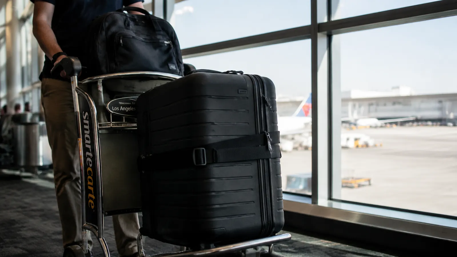 Black luggage strap buckled around a hard-shell suitcase on an airport luggage cart