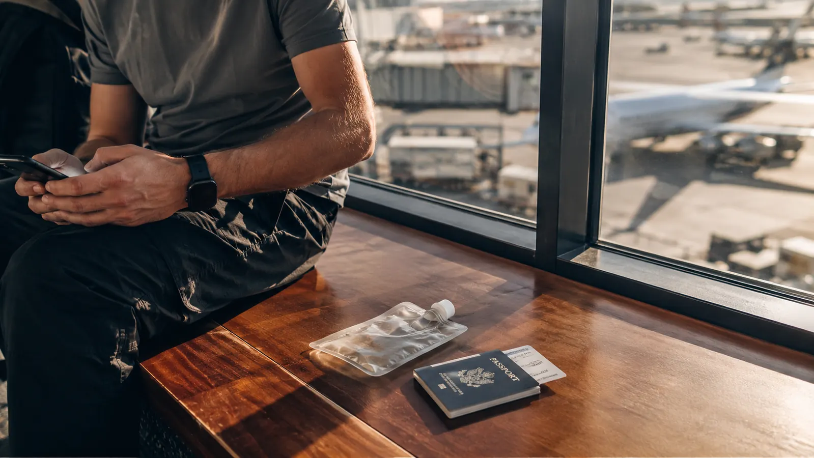 Collapsed clear travel water bottle sitting flat next to a passport and boarding pass on an airport bench