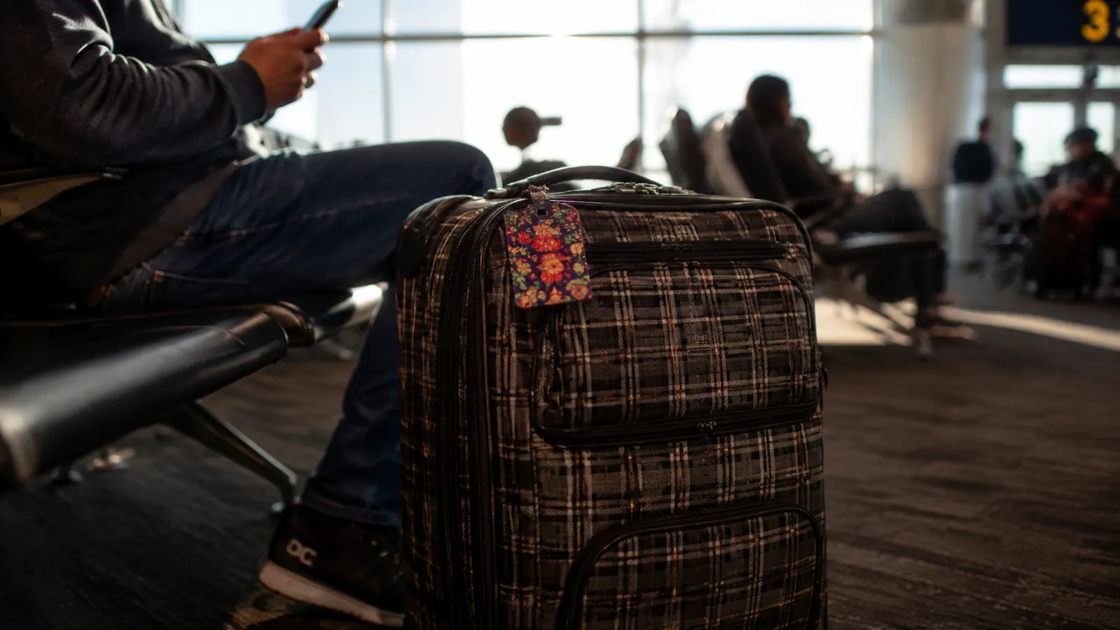 Bright teal luggage tag clipped to the handle of a checked suitcase at an airport gate